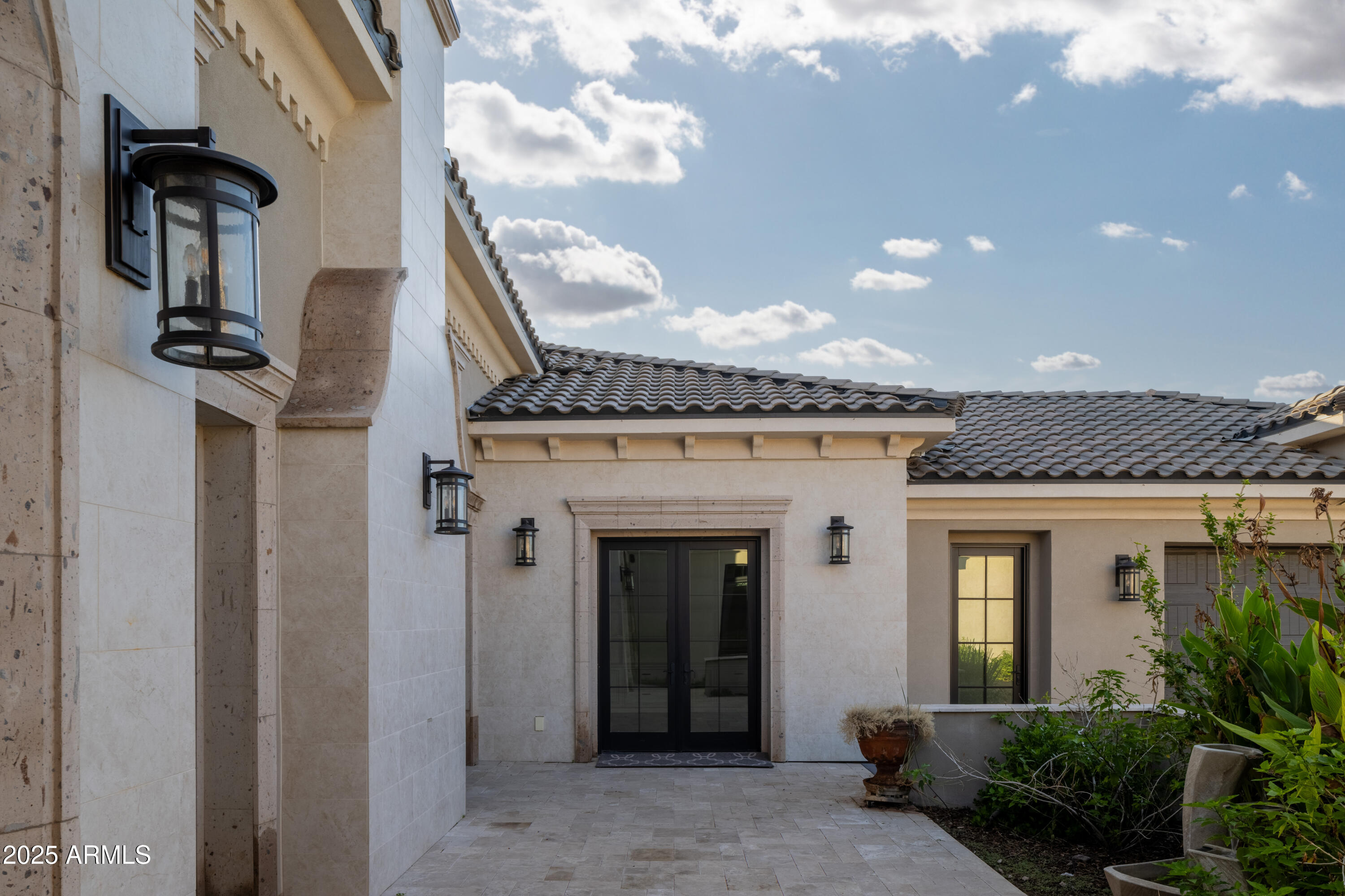 Stone-clad home entrance with black double doors, lanterns, tiled roof, and landscaped courtyard.