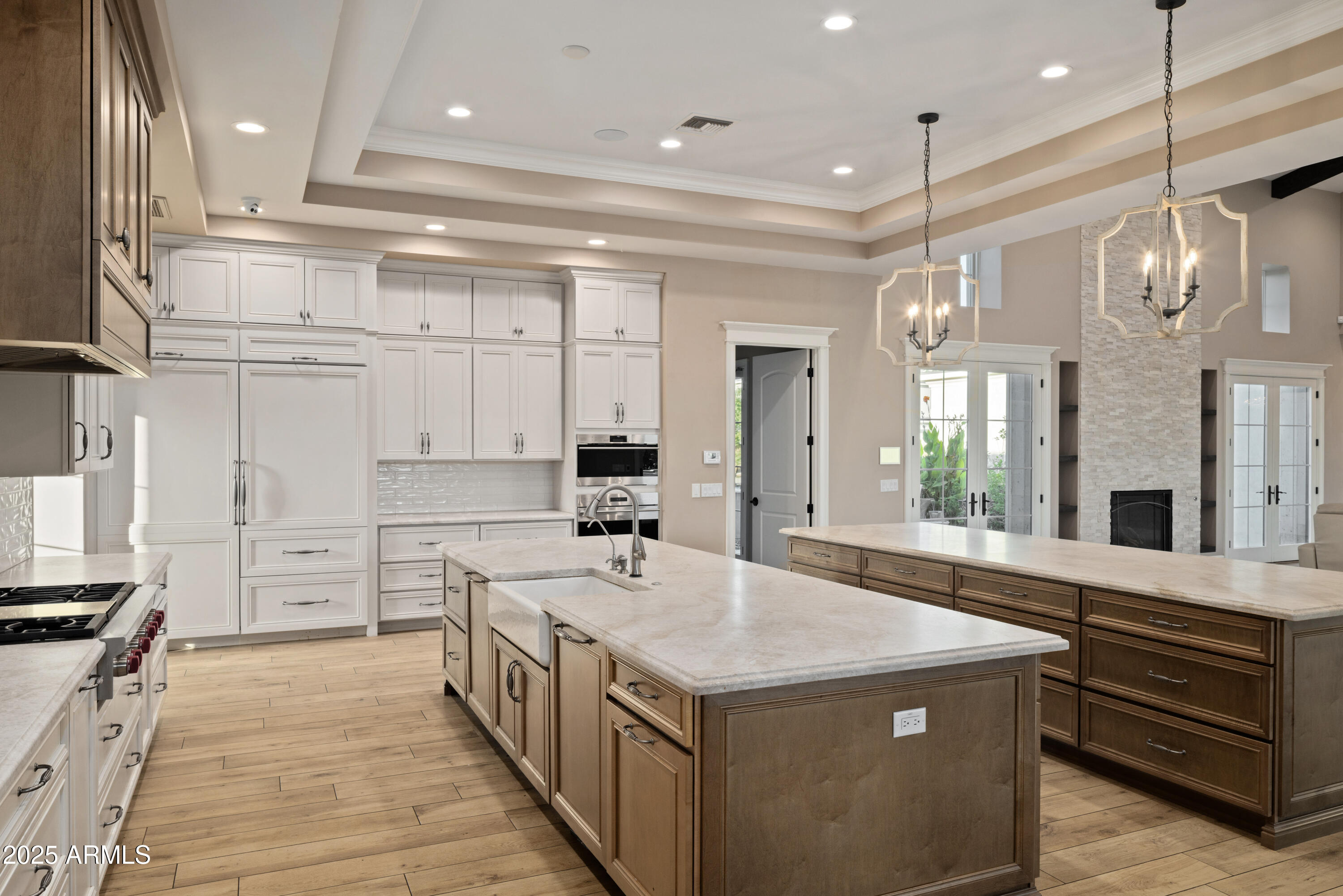 Kitchen with two stone-topped islands, white cabinetry, and an adjoining stone fireplace.