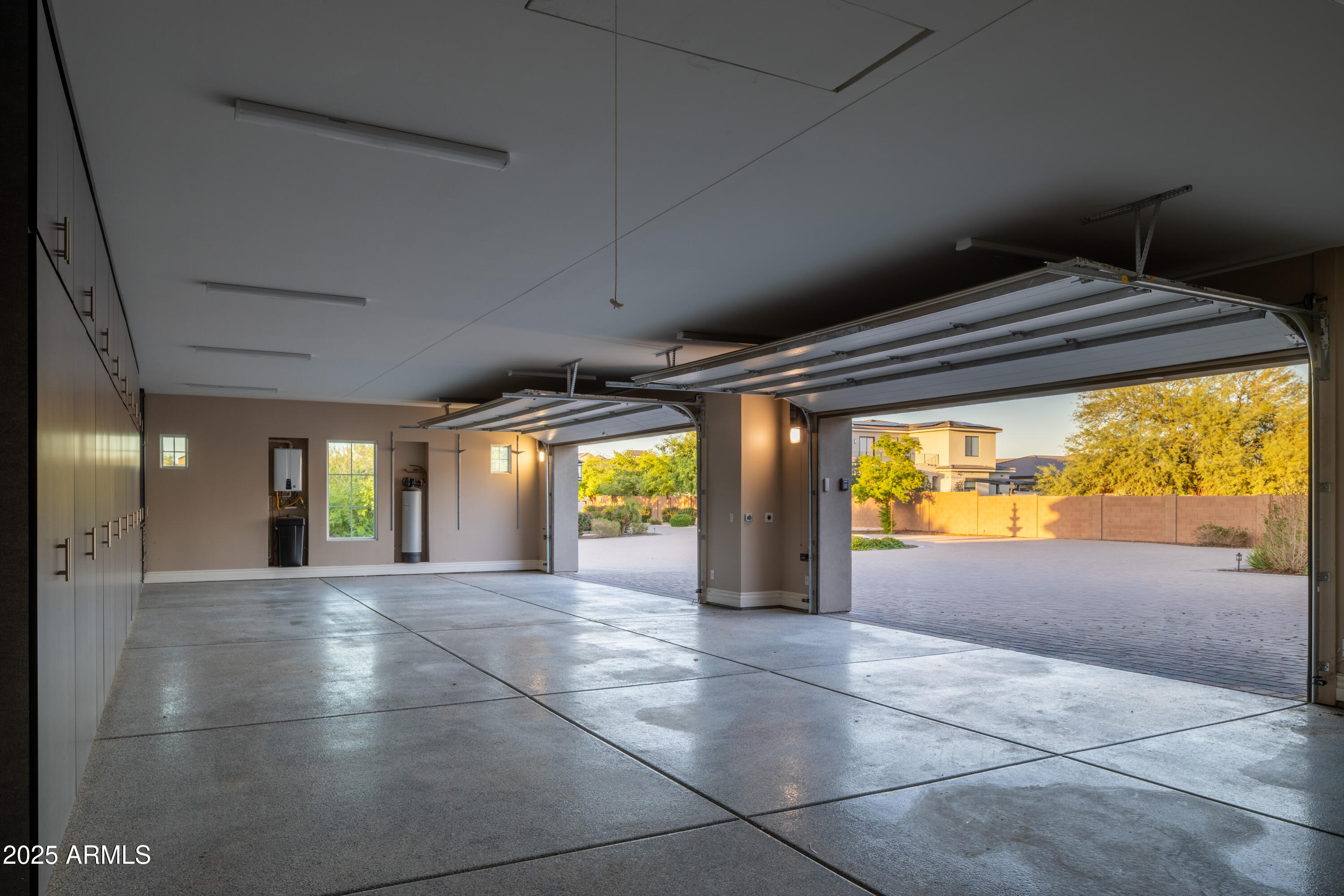 Spacious garage with built-in cabinets and two open doors overlooking a paved courtyard.