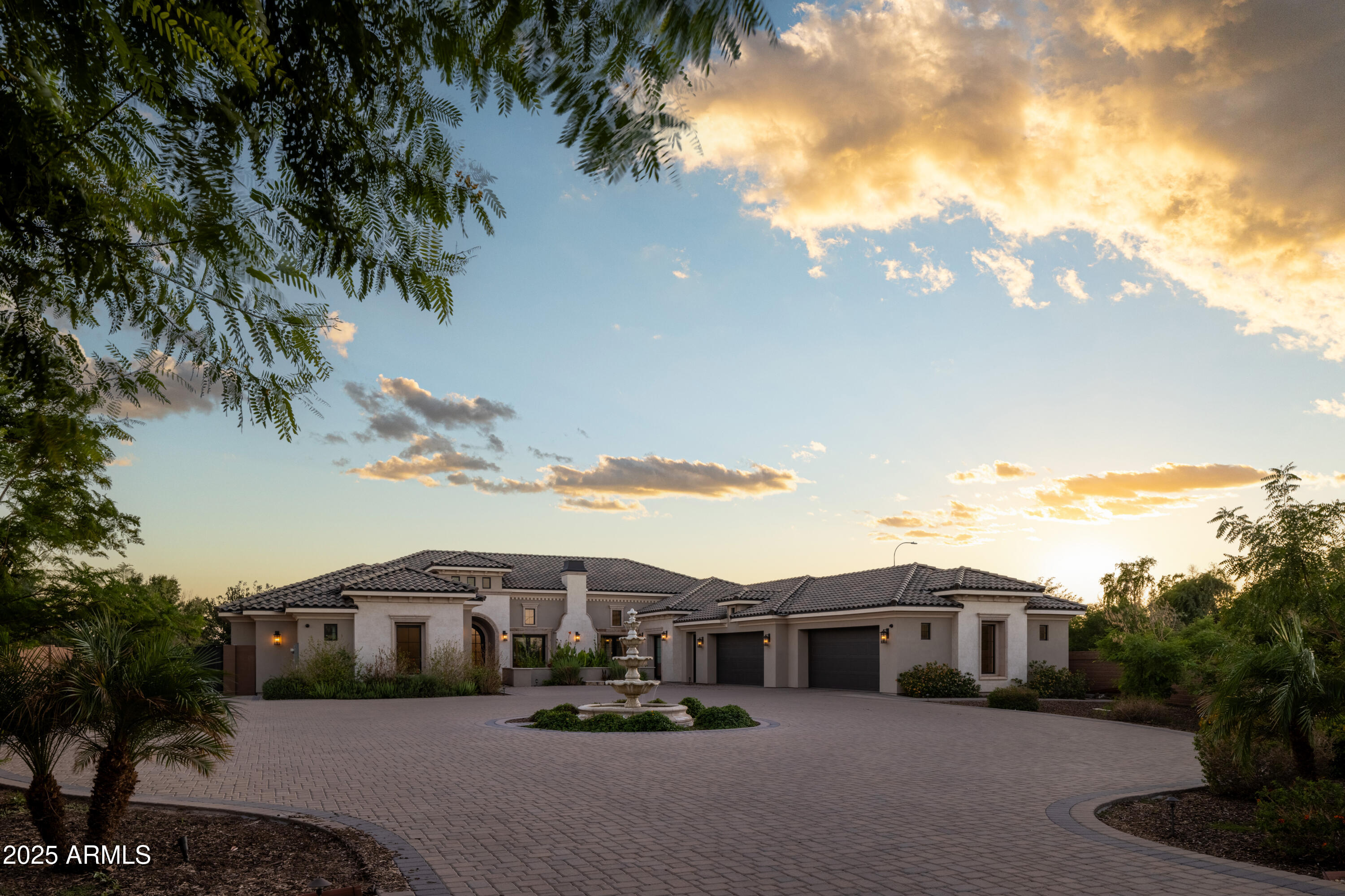 Large stucco home with tiled roof, twin garages, and courtyard fountain at dusk.