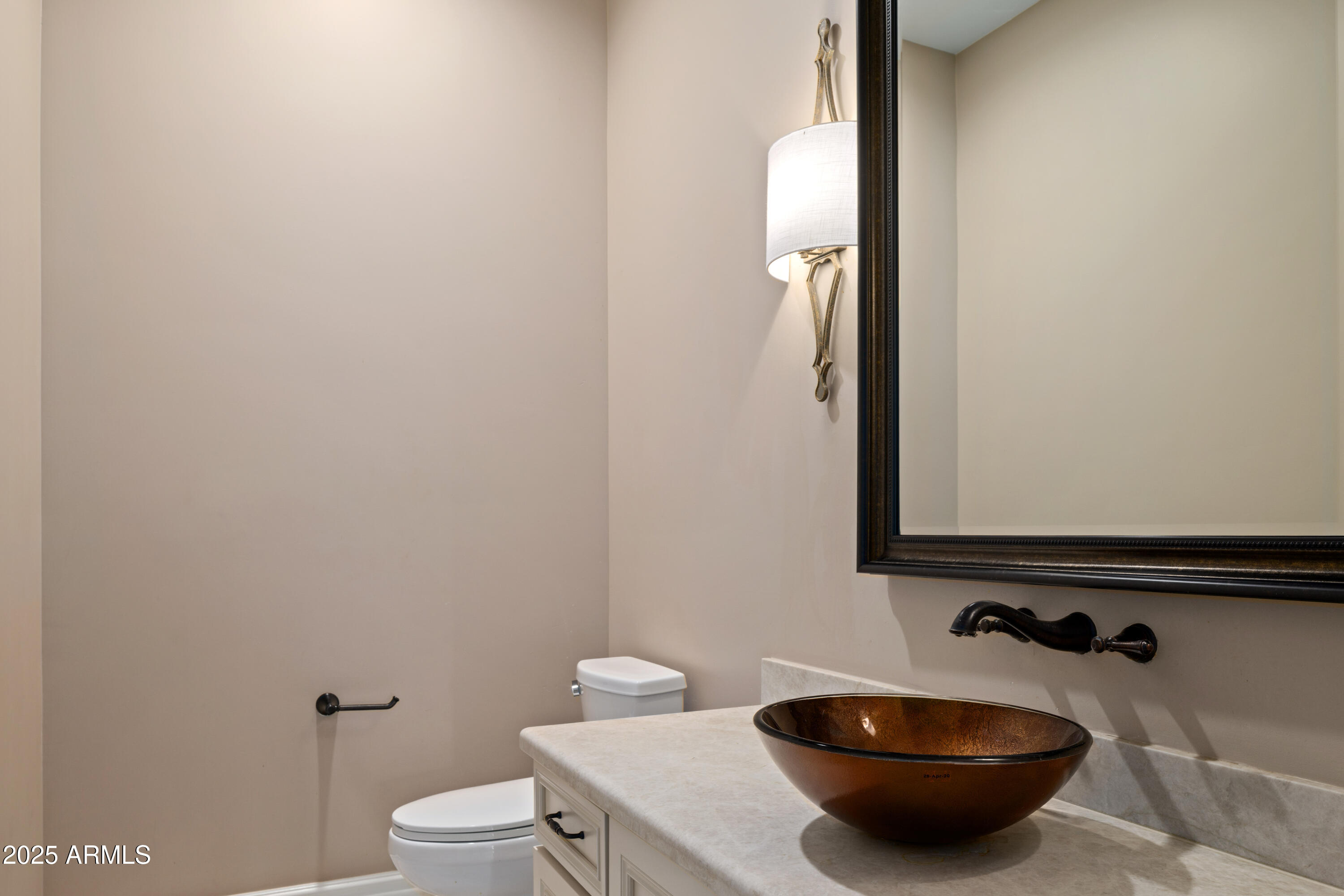Bathroom vanity with a brown vessel sink, large framed mirror, and wall sconce.