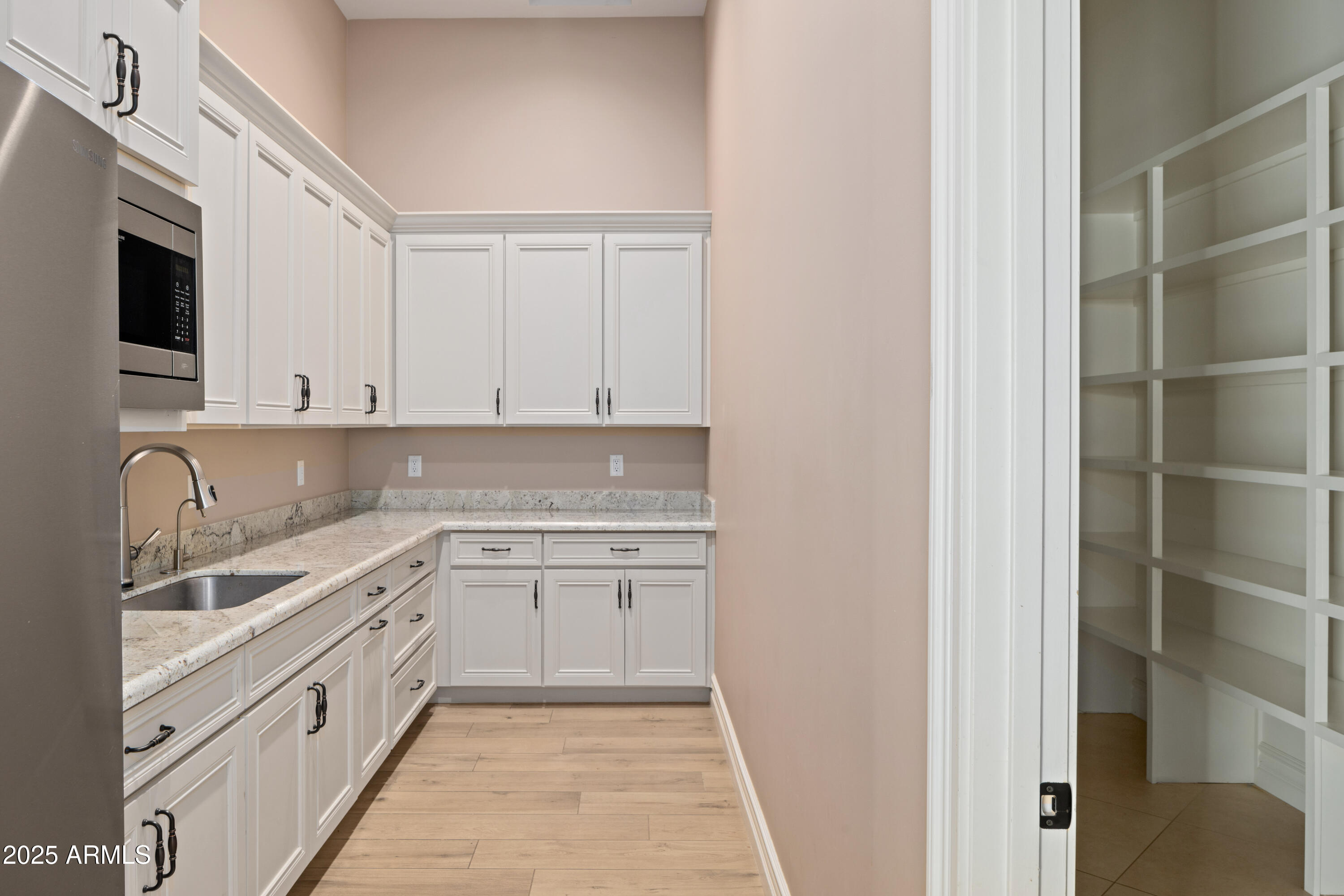 Kitchen with white cabinets, stone counters, stainless-steel appliances, and a doorway to built-in shelving.