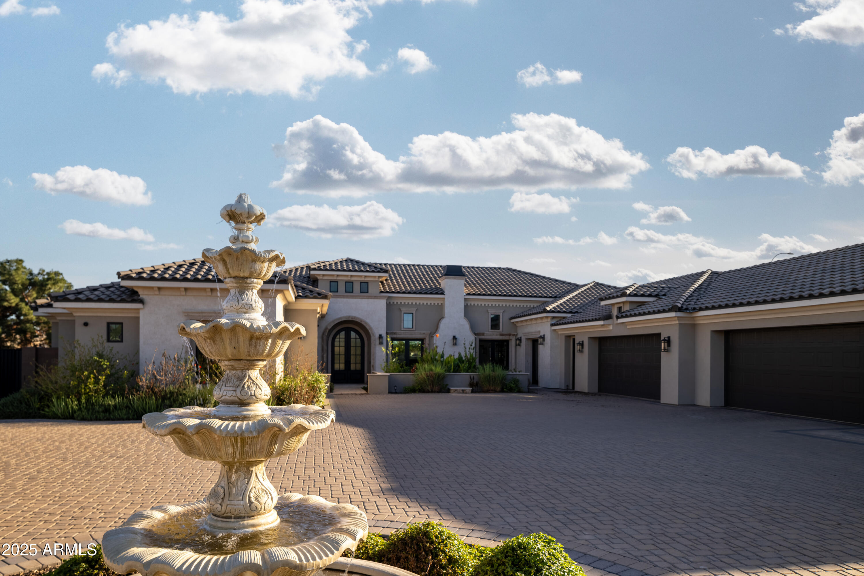 Large stucco home with tiled roofs and multiple garages behind a tiered fountain in the courtyard.