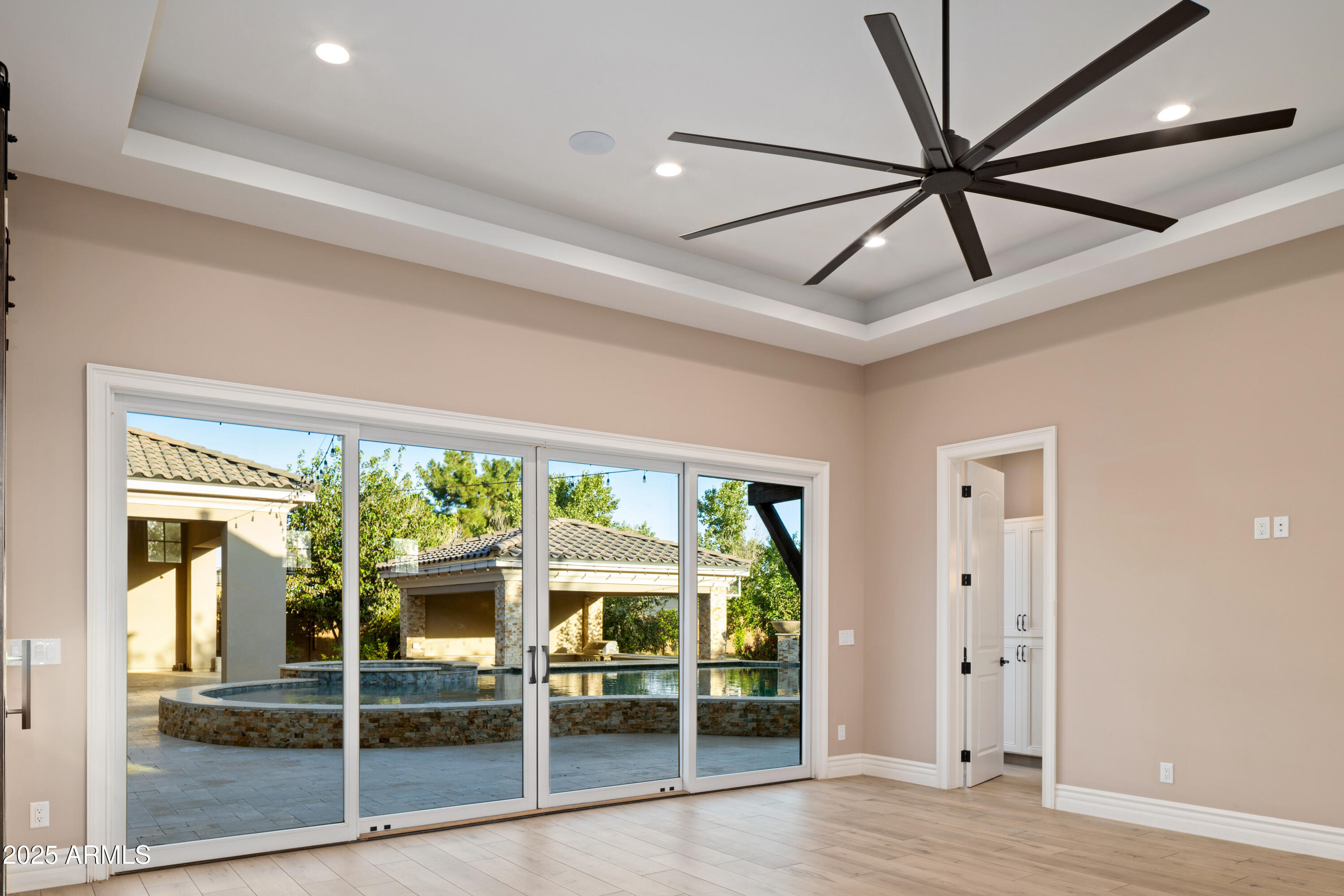 Empty room with a large ceiling fan and sliding doors overlooking a pool and raised spa.