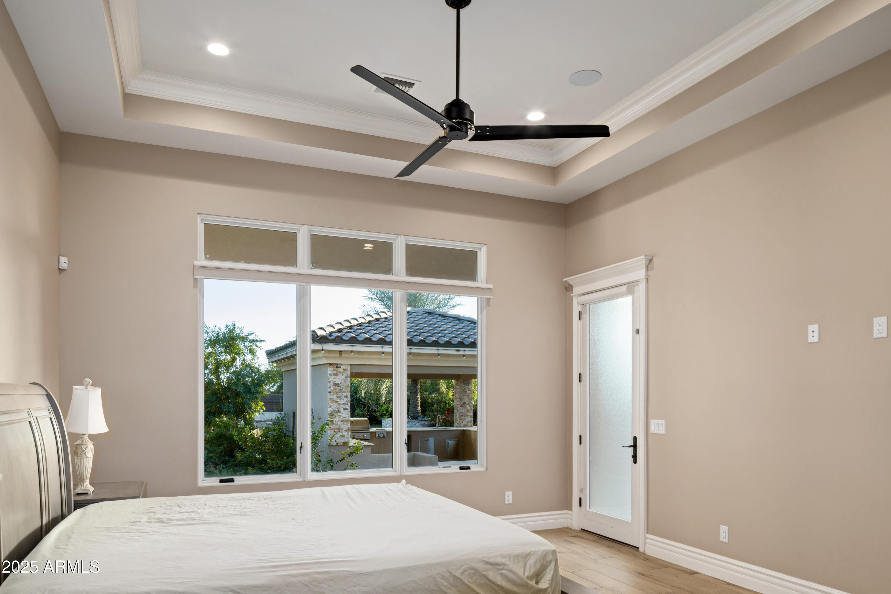 Bedroom with a tray ceiling, large window, and glass door overlooking a covered patio.