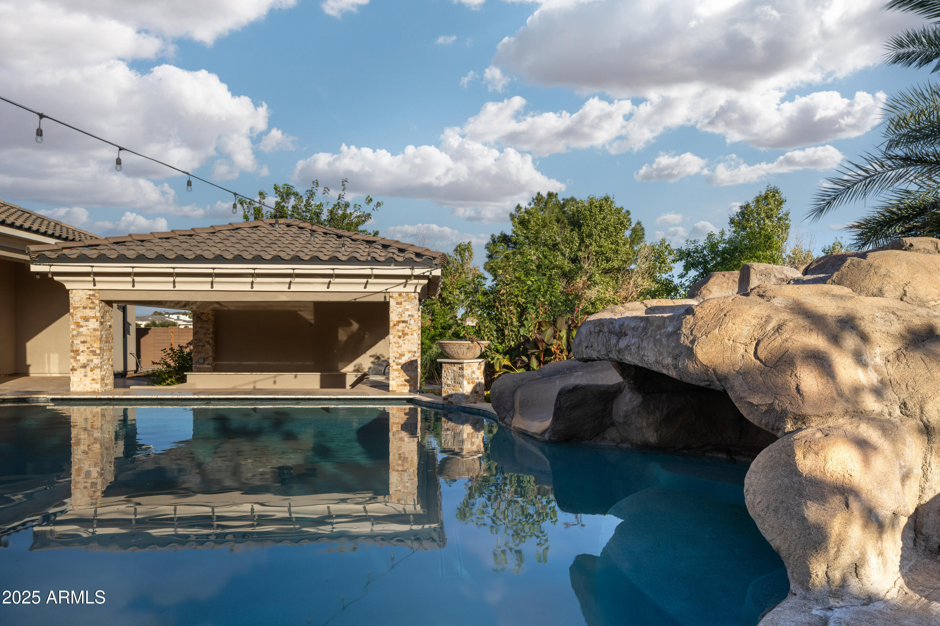 Backyard swimming pool with a large rock waterfall beside a covered patio.
