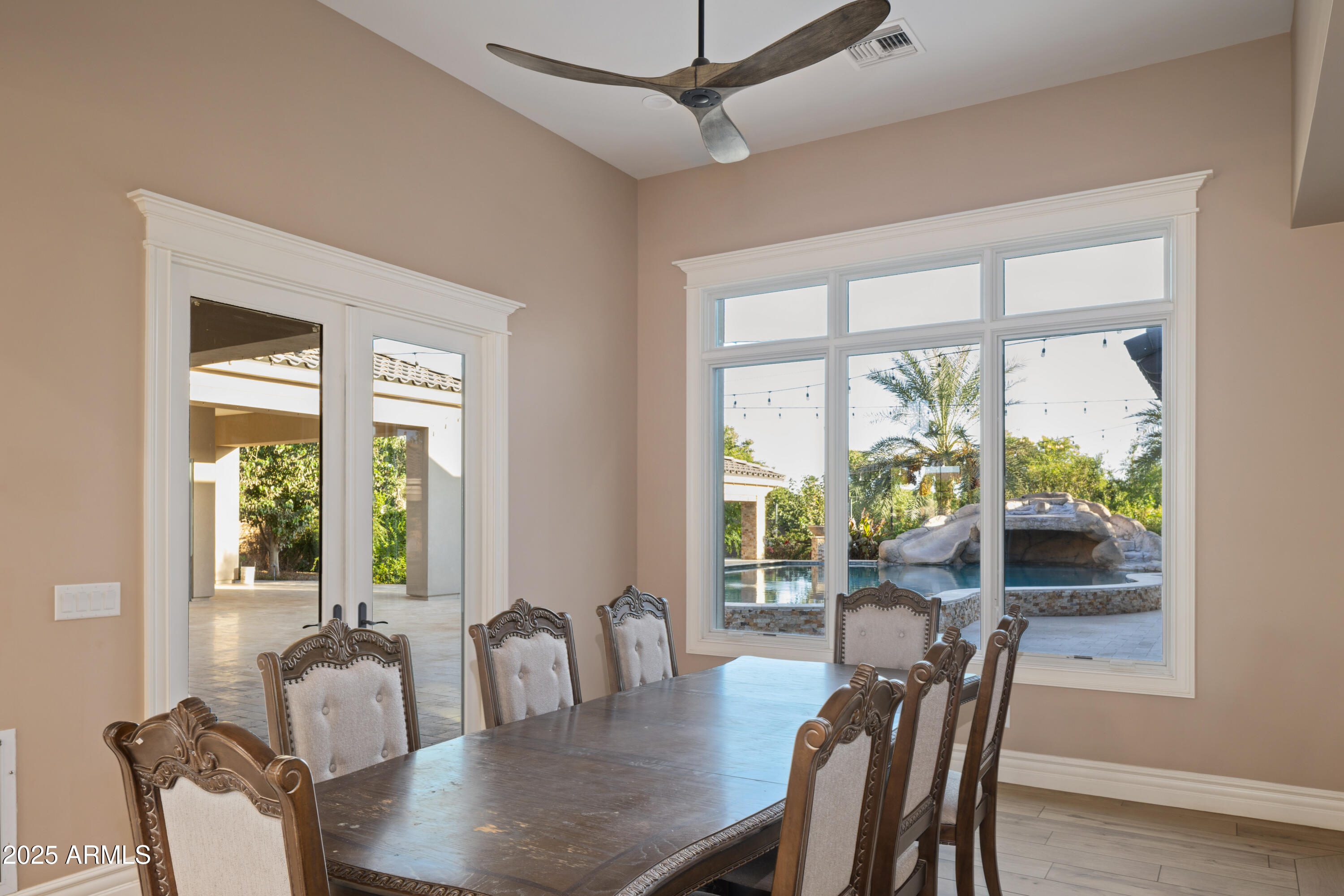 Dining room with an ornate wood table overlooking a backyard pool through wide windows.