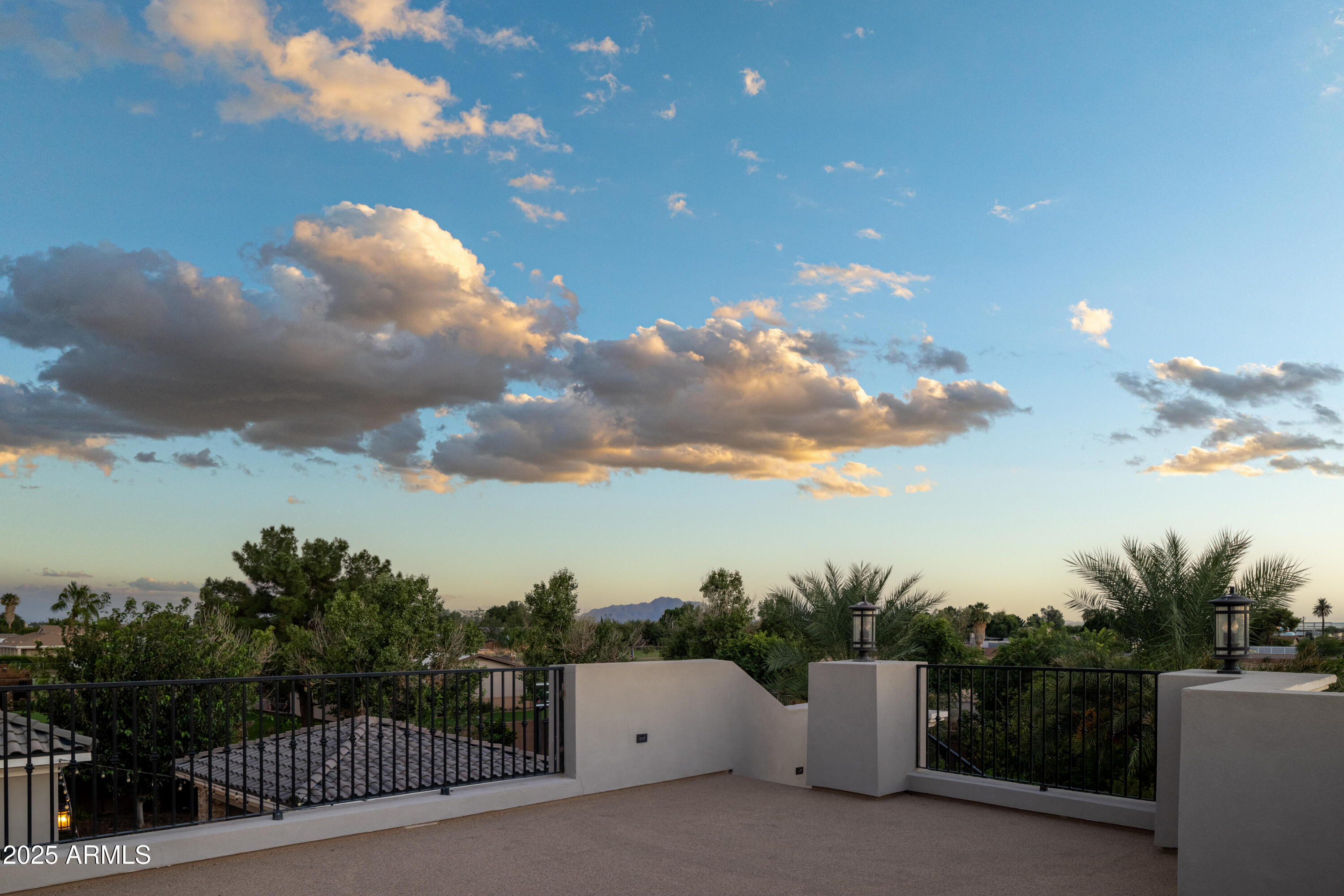 Rooftop terrace overlooking treetops and distant mountains beneath dramatic golden-hour clouds.
