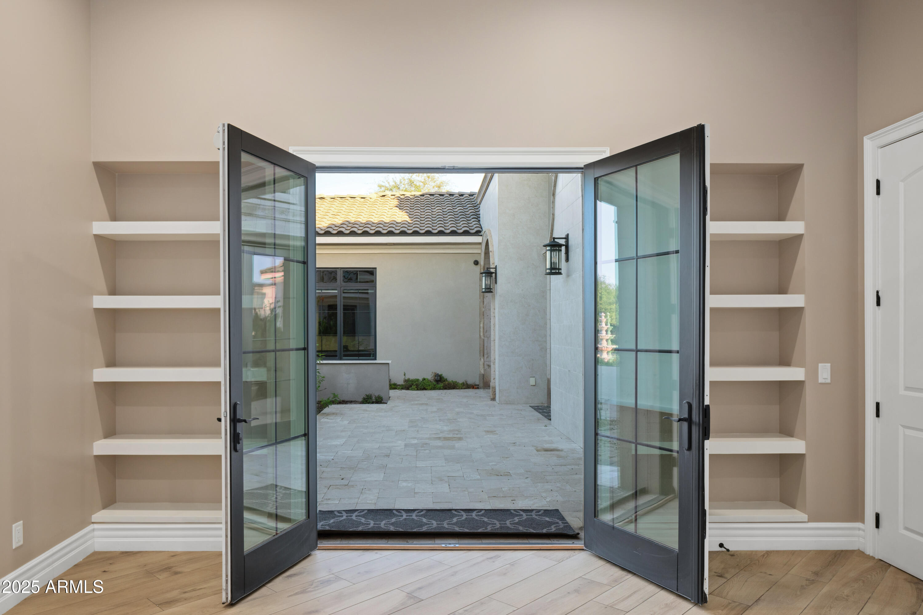 Open glass doors lead from a room with built-in shelves to a tiled courtyard.