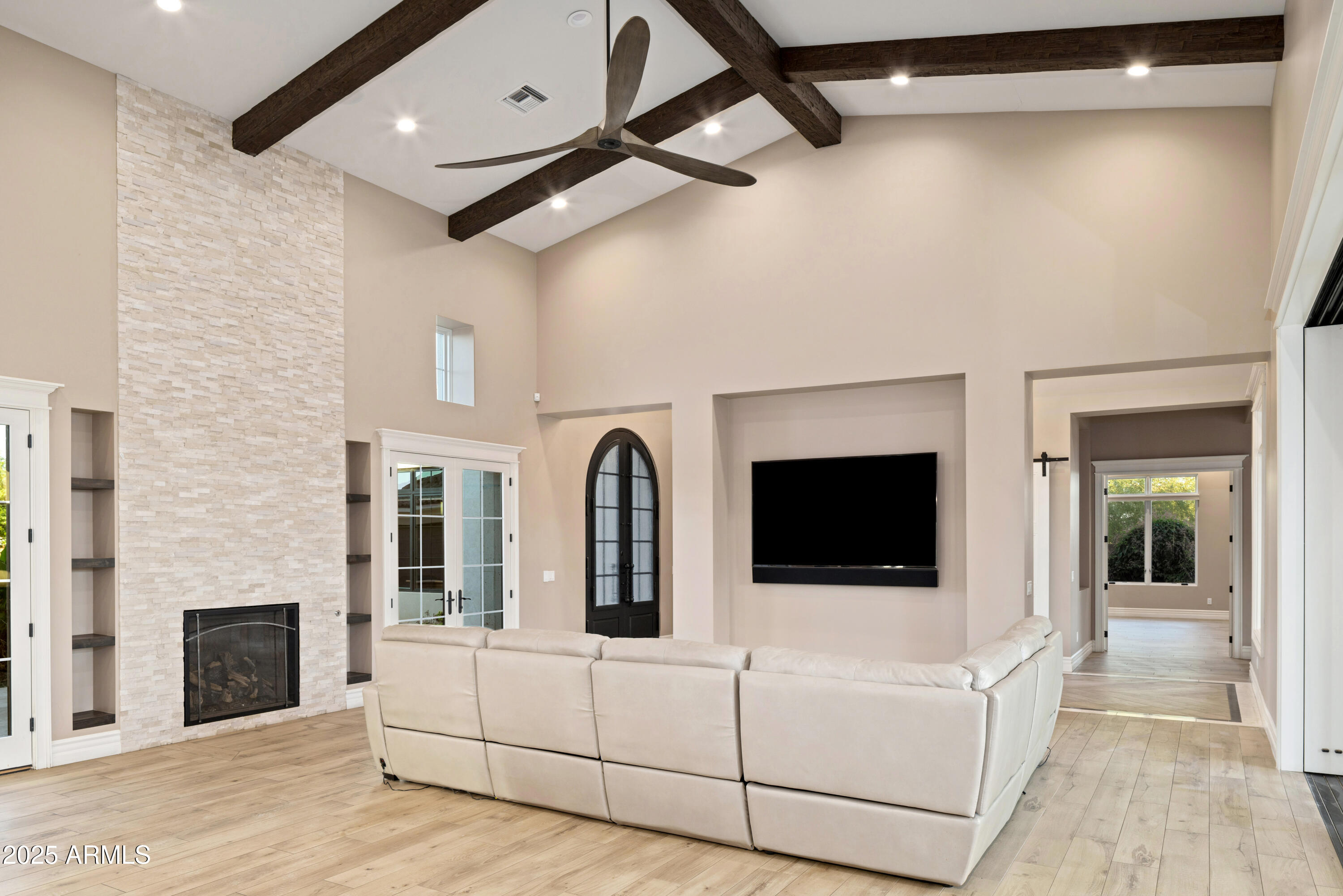 Living room with vaulted wood-beam ceiling, stone fireplace, white sectional, and wall-mounted television.