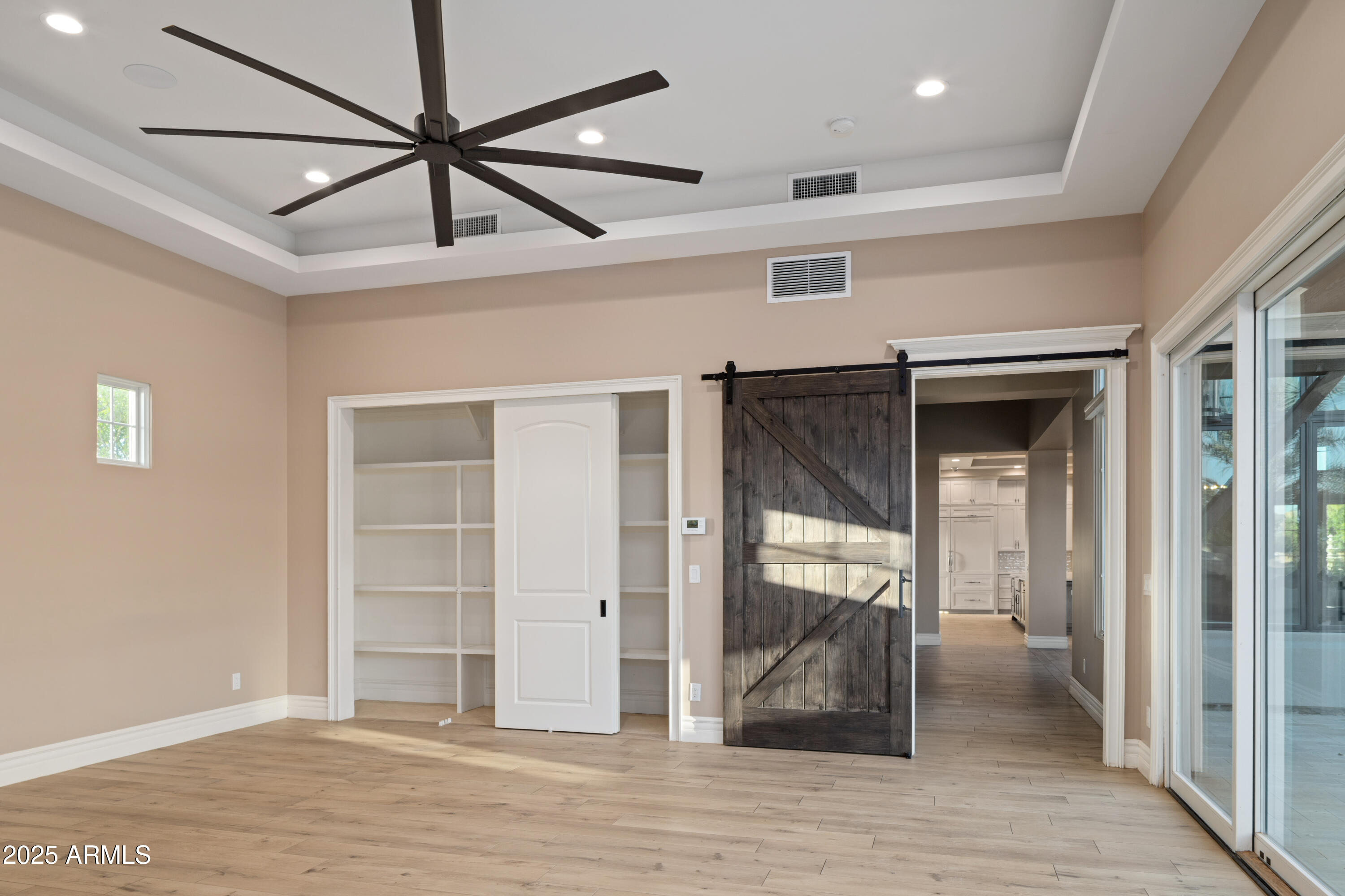 Empty room with built-in shelving, a dark barn door, and glass sliding doors.