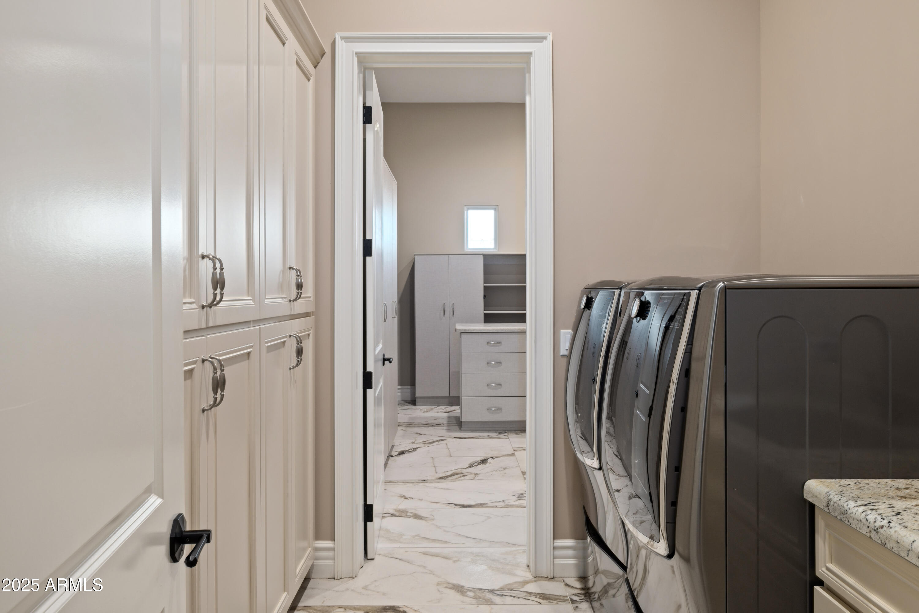 Laundry room with front-loading washer and dryer, white cabinets, and marble-look tile flooring.