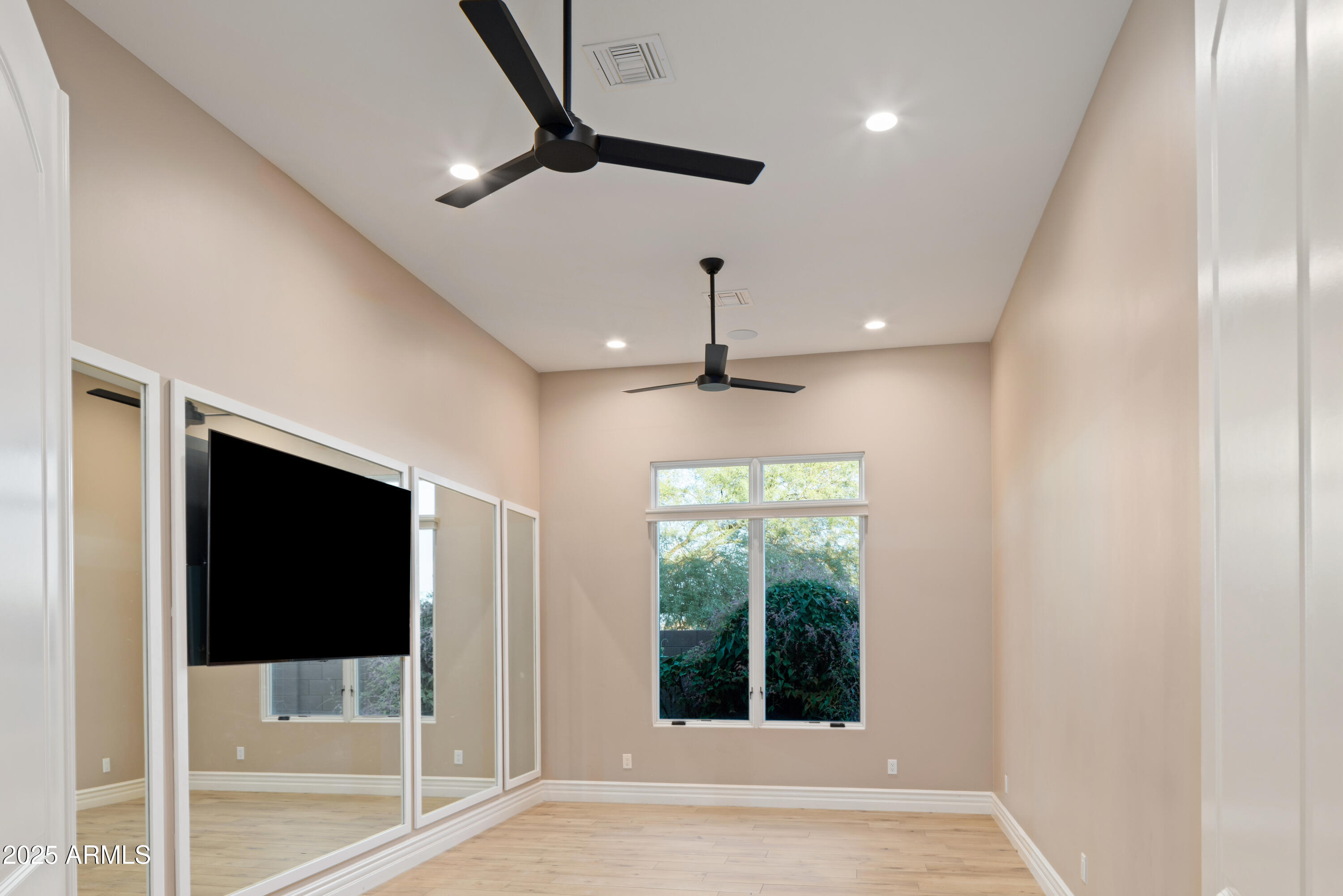 Empty bedroom with mirrored closet doors, a mounted television, and two ceiling fans.