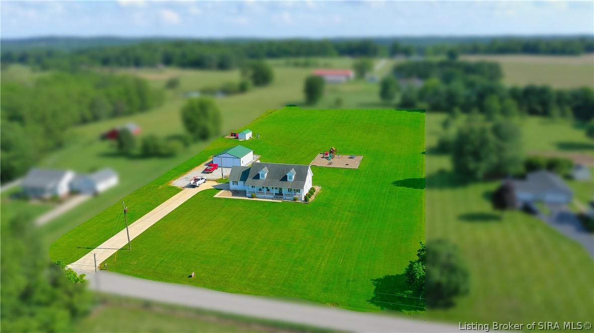 Aerial view of a rural home with a long driveway, large lawn, detached outbuilding, and play area.