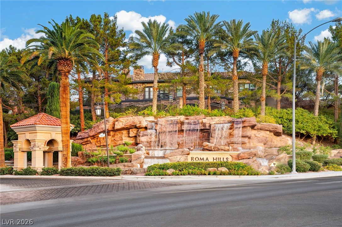 Roma Hills entrance with a stone waterfall, landscaped grounds, and tall palm trees.