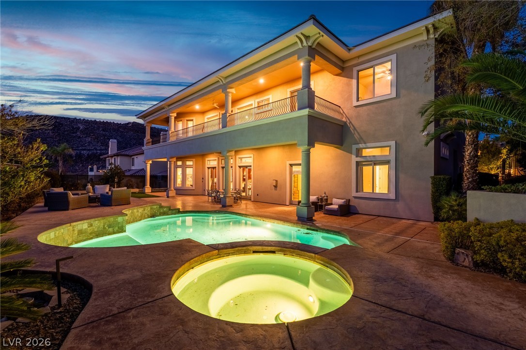 Two-story home with an illuminated backyard pool, circular spa, and covered balcony at dusk.