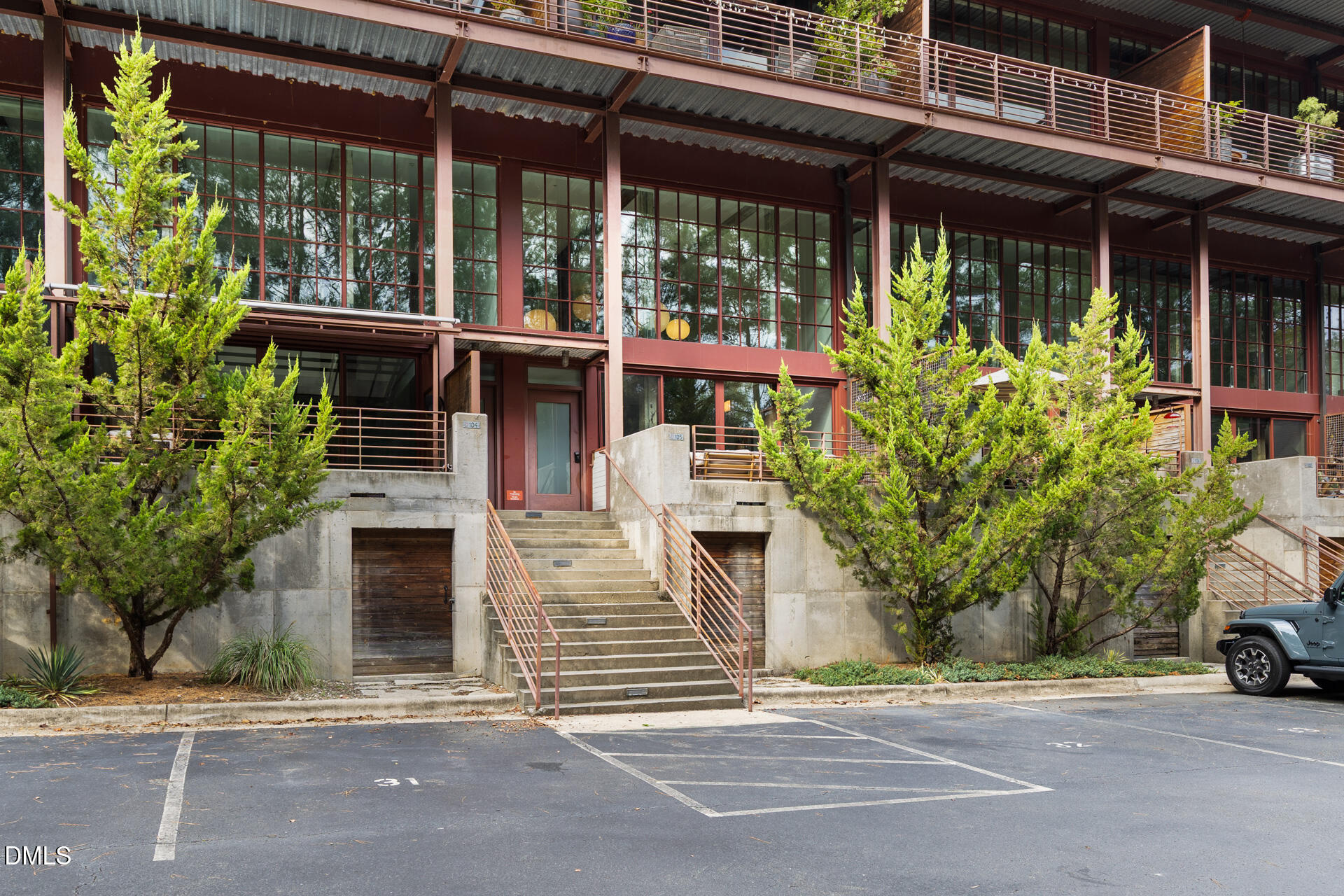 Modern multi-story residential building with metal balconies, broad concrete stairs, and trees along the frontage.