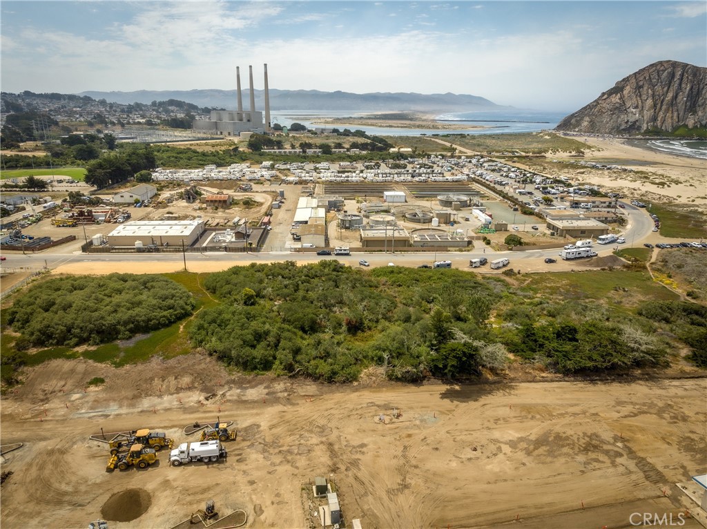 Aerial view of graded coastal land with earthmoving equipment, brush, and the bay beyond.