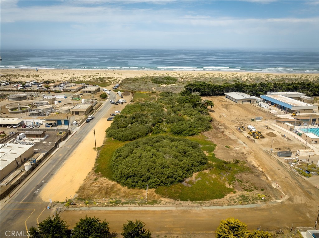 Aerial view of vacant coastal land with brush, nearby buildings, and the ocean beyond.