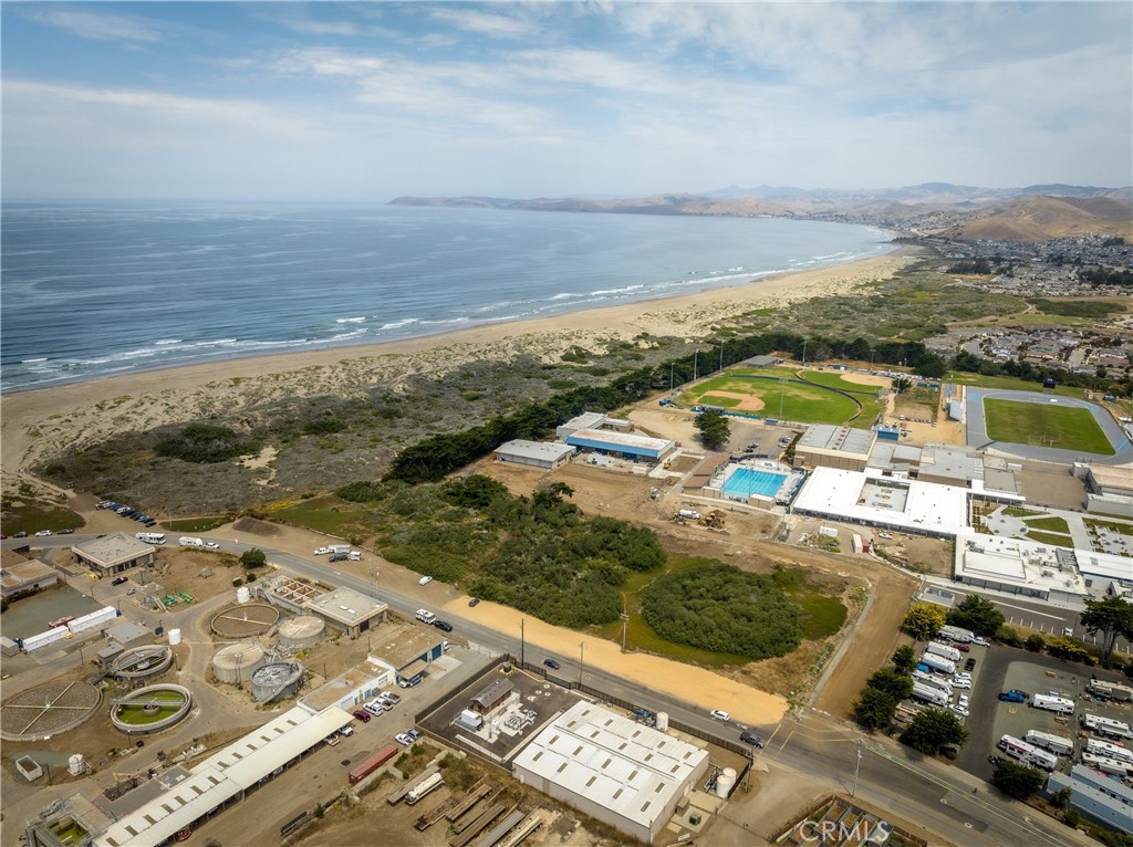 Aerial coastal view with a sandy beach, ocean, sports fields, and nearby buildings.