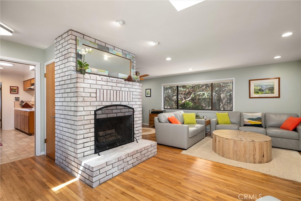 Living room with a white brick fireplace, hardwood floors, and gray sectional beside a large window.