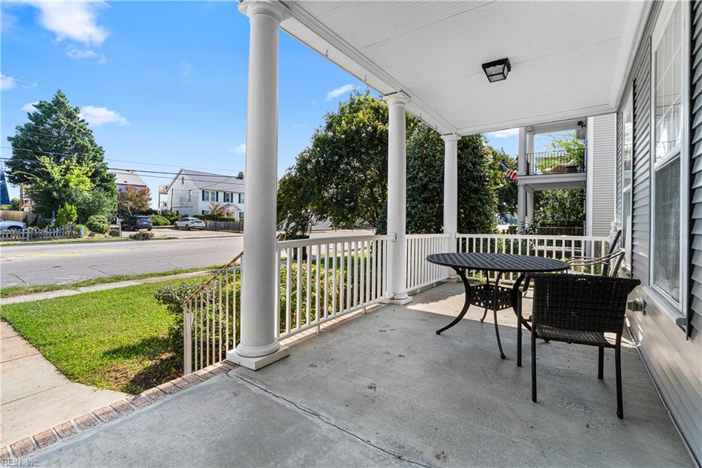 Covered front porch with white columns and black patio furniture facing a residential street.