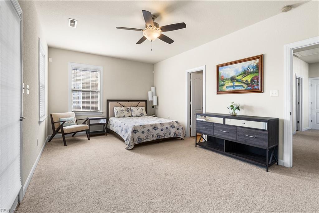 Furnished bedroom with a patterned bed, beige carpet, ceiling fan, and dark dresser.