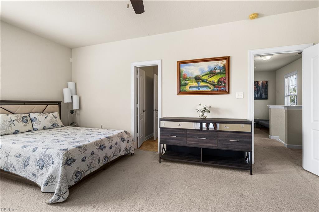 Bedroom with a seashell-patterned bedspread, dark dresser, and landscape painting.