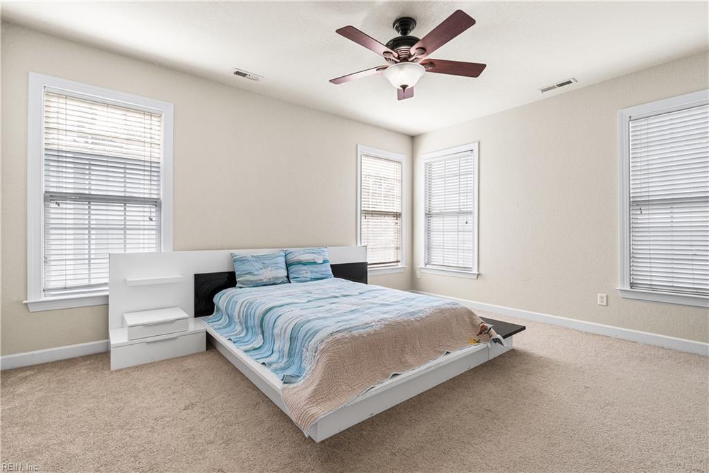 Furnished bedroom with a low platform bed, blue bedding, and windows with white blinds.