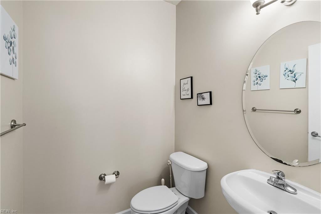 Bathroom with a white toilet, pedestal sink, oval mirror, and botanical wall art.