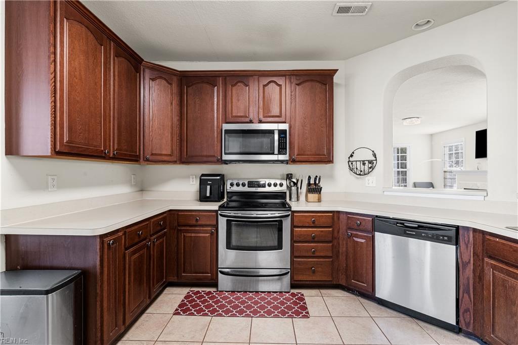Kitchen with dark wood cabinets, stainless steel appliances, and light tile flooring.