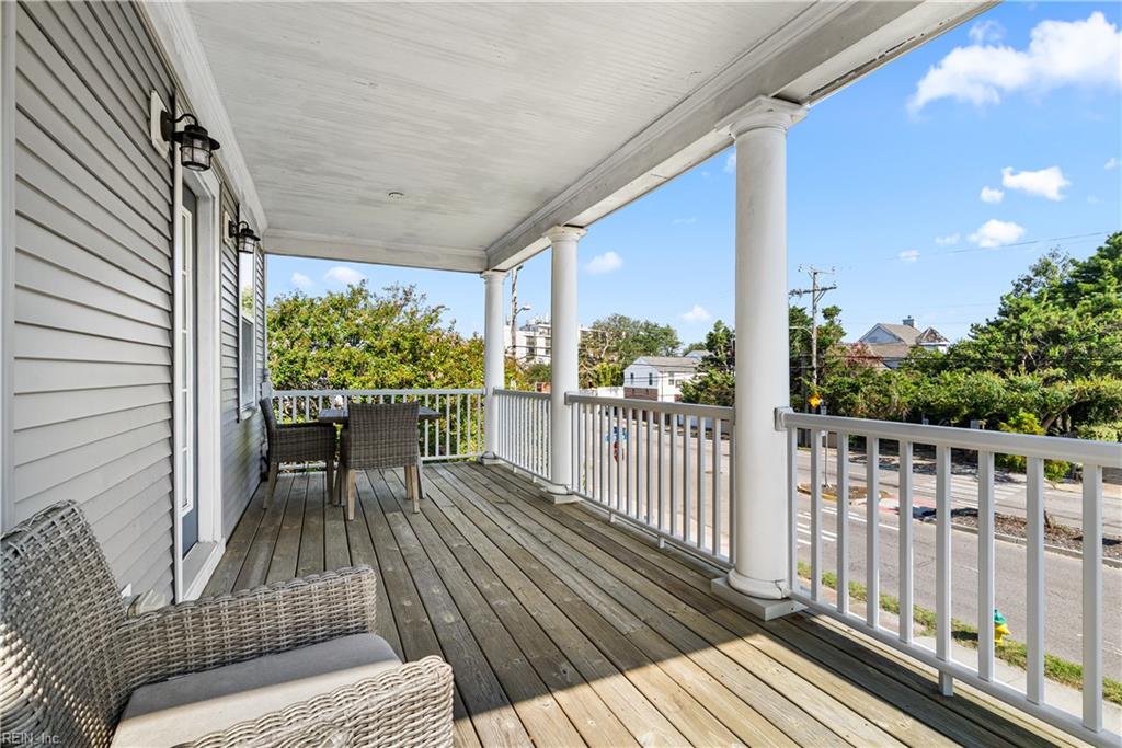 Covered wooden porch with white columns, wicker seating, and a view of the street.