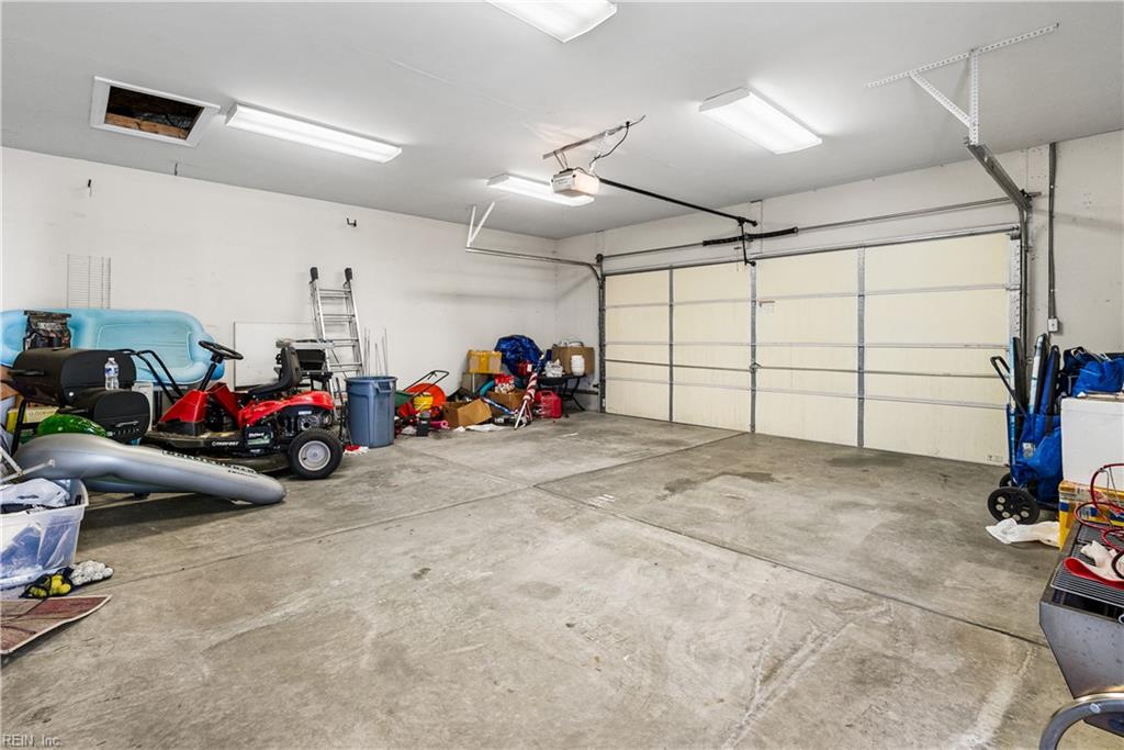 Spacious garage with a large sectional door, concrete floor, and stored lawn equipment.