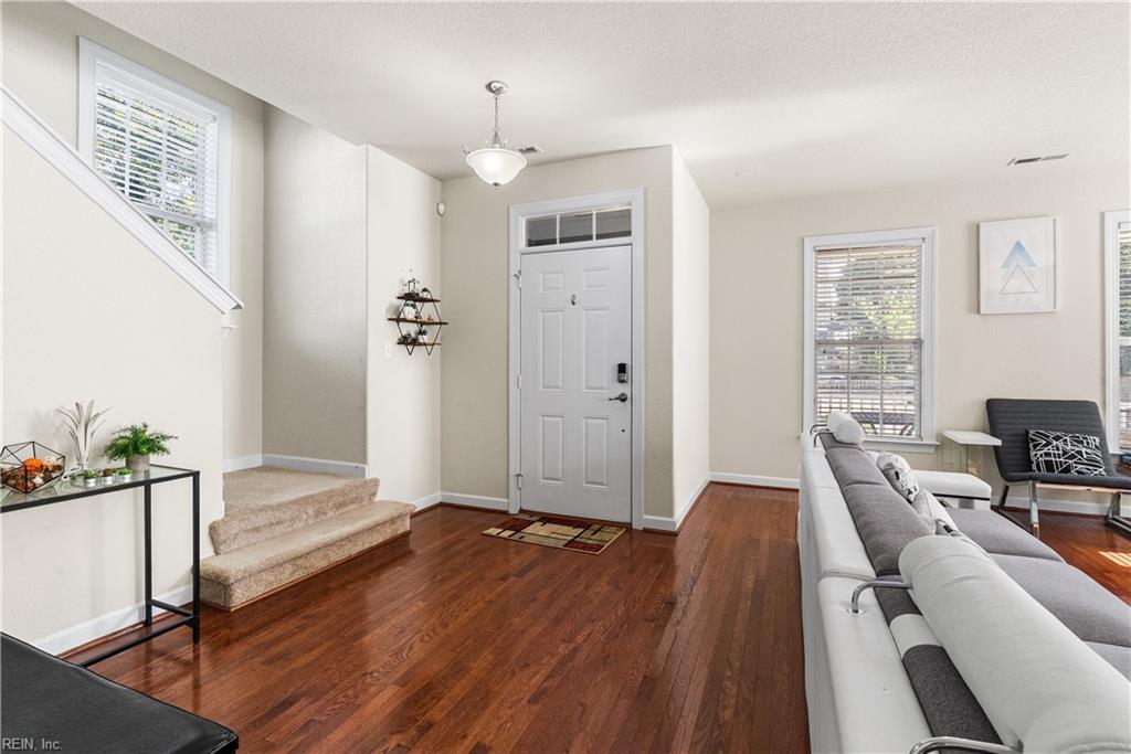 Living room with hardwood floors, carpeted stairs, and a white front door.