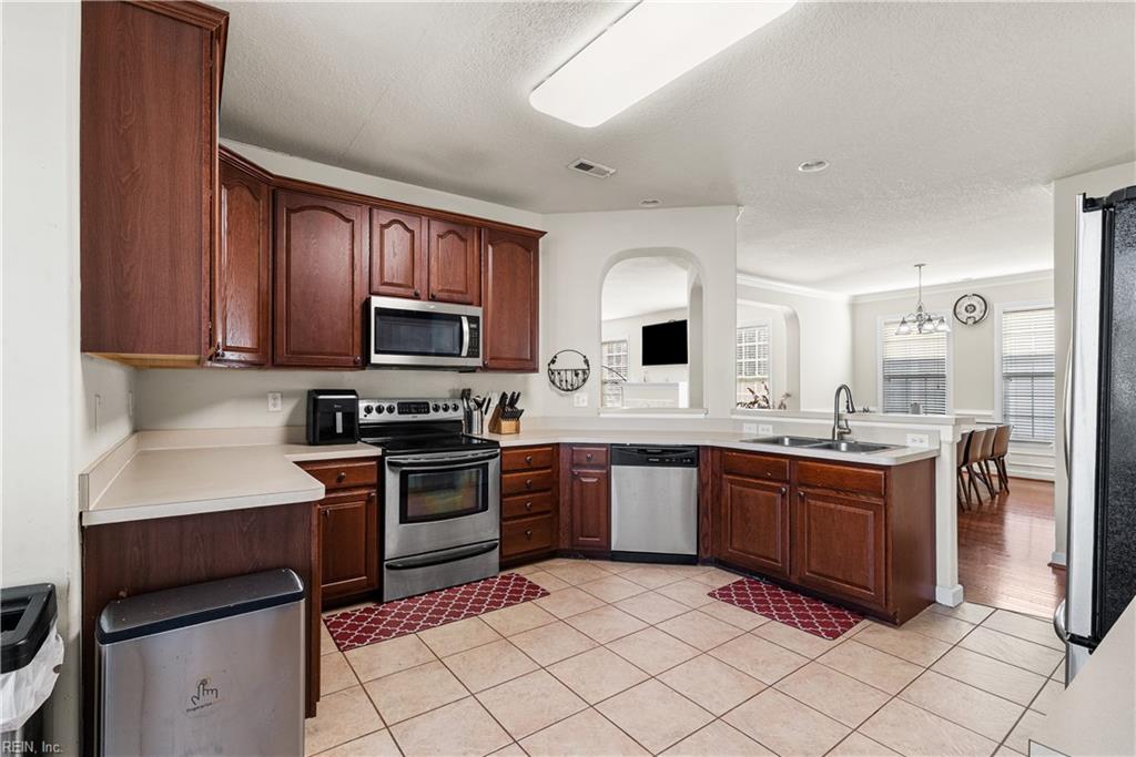 Kitchen with dark wood cabinets, stainless steel appliances, and a peninsula sink opening to the dining area.