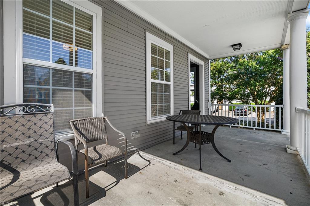 Covered porch with a round metal table and chairs beside gray siding and white-trimmed windows.