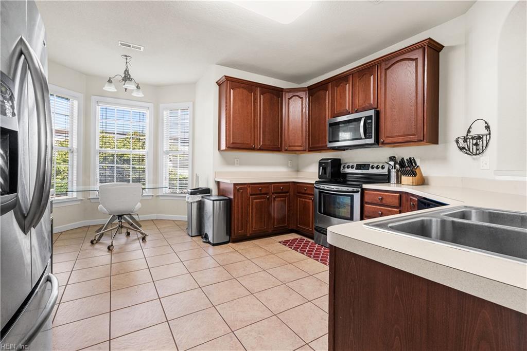 Kitchen with dark wood cabinets, stainless steel appliances, and a desk area beside three windows.