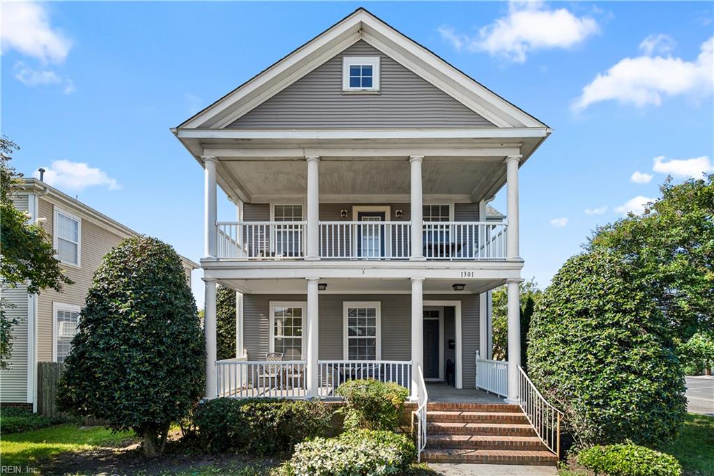 Gray two-story house with white-columned porches on both levels and brick front steps.
