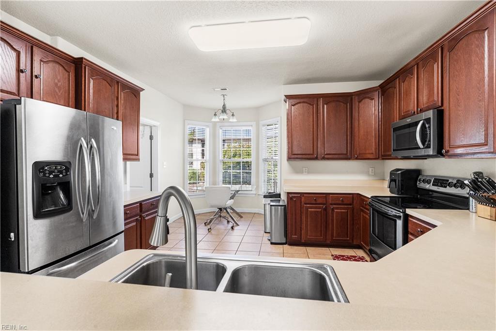 Kitchen with reddish-brown cabinets, stainless steel appliances, a double sink, and bay windows.