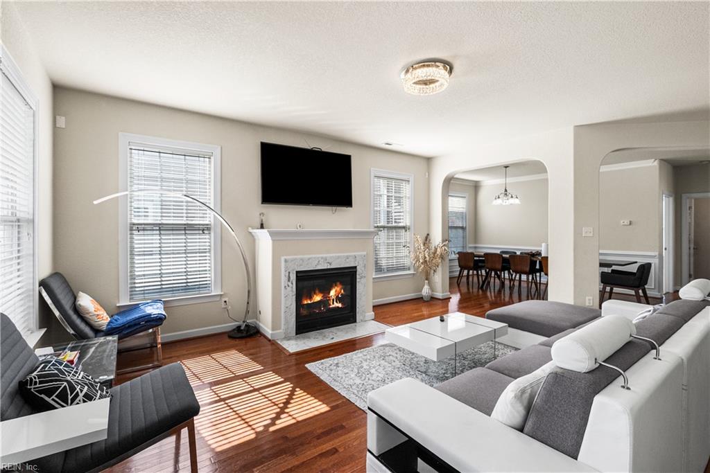 Living room with a fireplace, hardwood floors, gray seating, and an open dining area.