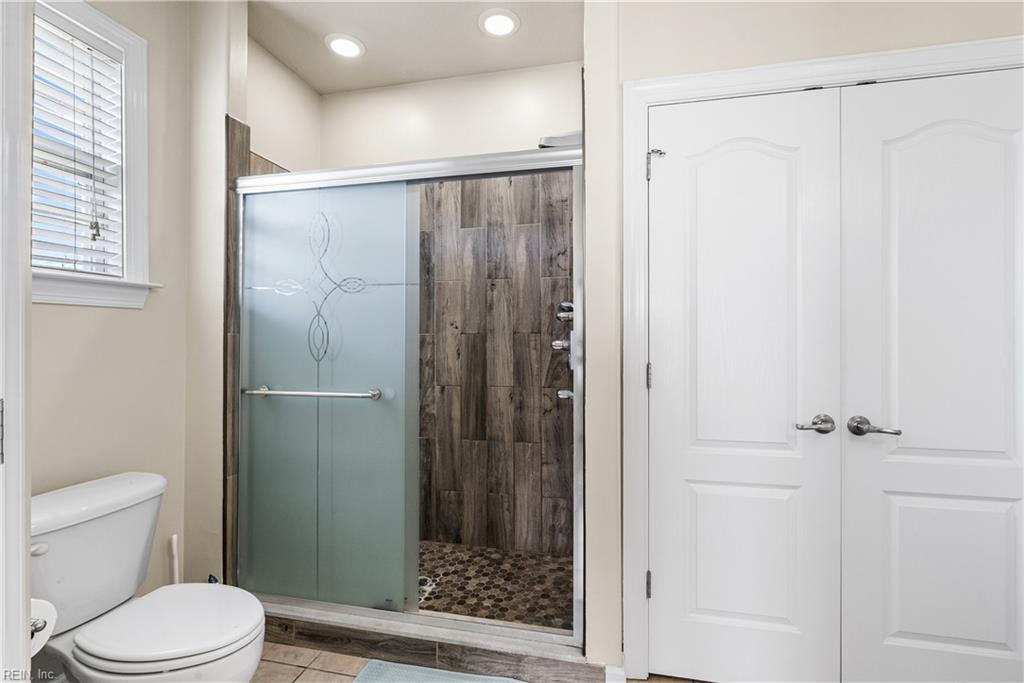 Bathroom with a glass shower, dark wood-look tile, pebble floor, and white double doors.