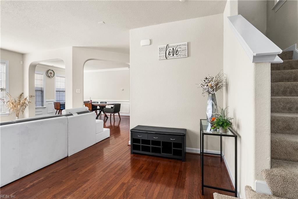 Open-plan living and dining area with reddish hardwood floors, arched openings, and a carpeted staircase.