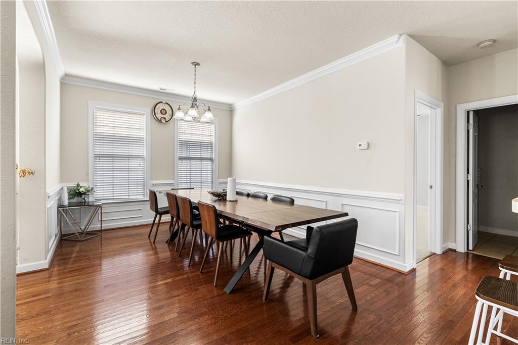 Dining room with a long wooden table, hardwood floors, white wainscoting, and chandelier.