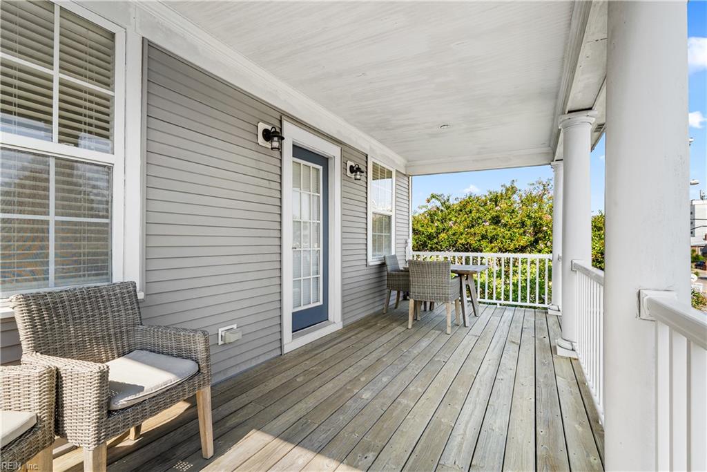 Covered porch with wicker seating, gray siding, white railings, and weathered wood decking.
