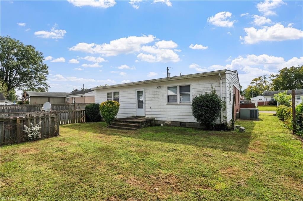 Rear of a single-story white-sided house with a grassy backyard and wooden fence.