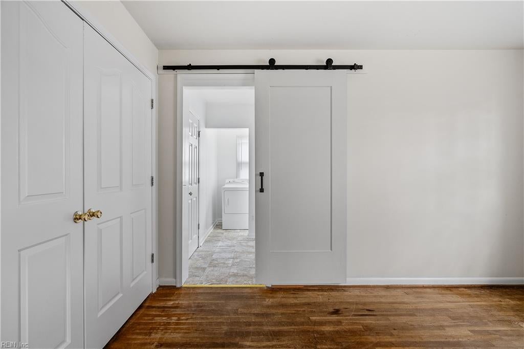 Unfurnished room with hardwood floors and a sliding barn door opening to a laundry area.