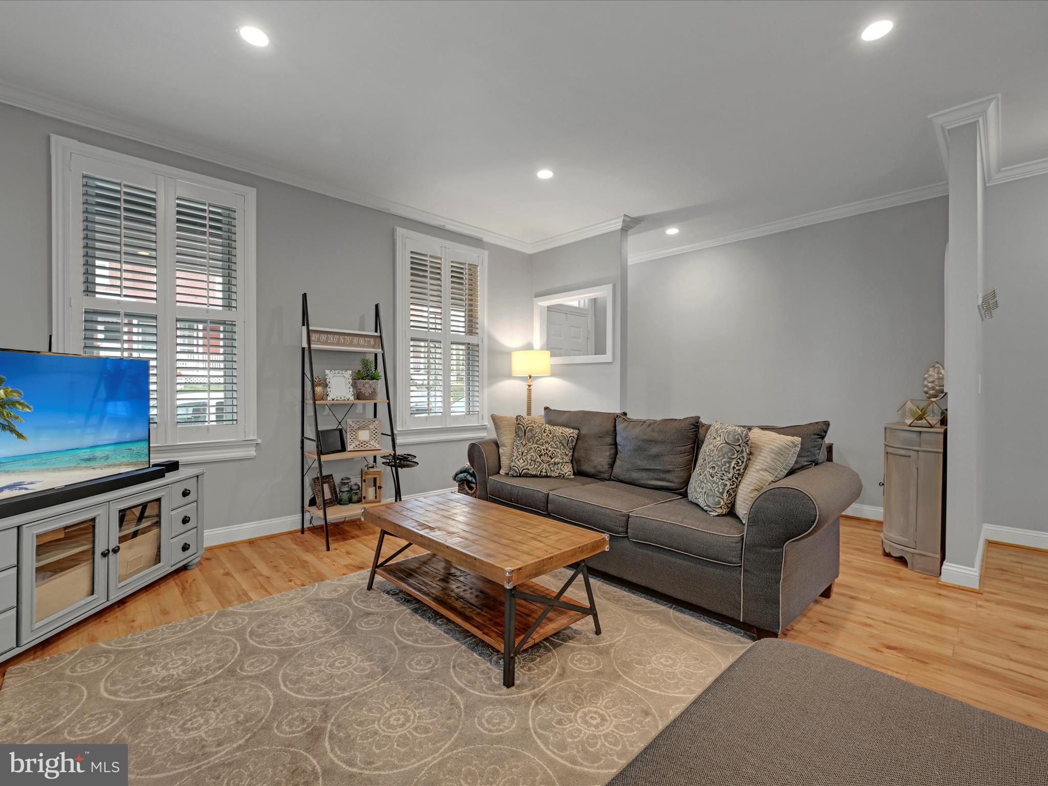 Furnished living room with a gray sofa, wooden coffee table, and plantation-shuttered windows.
