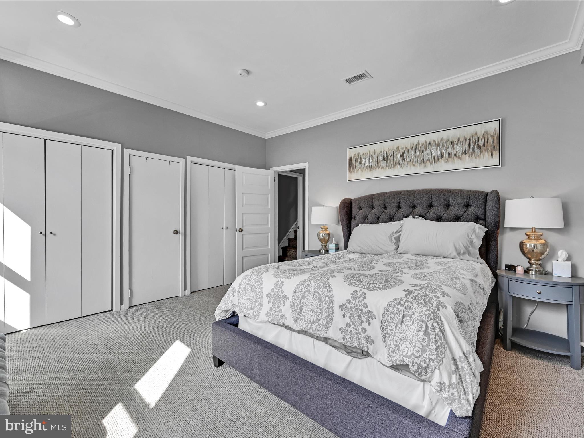 Furnished bedroom with a gray upholstered bed, patterned bedding, and multiple closets.