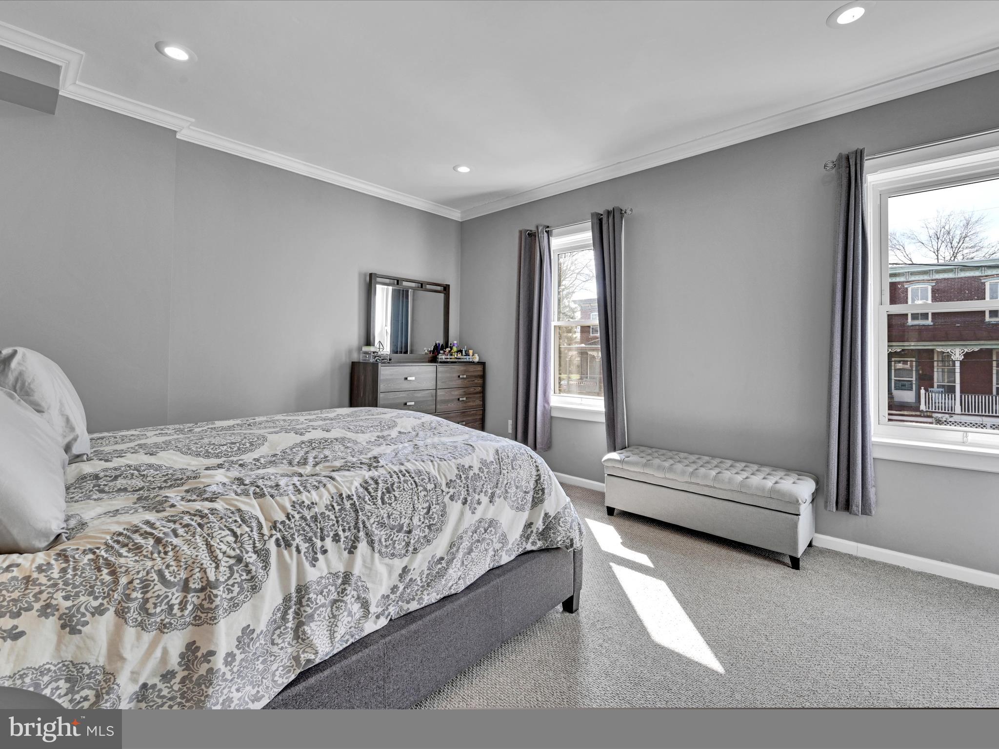 Bedroom with a patterned bedspread, gray walls, and a tufted bench beneath two windows.