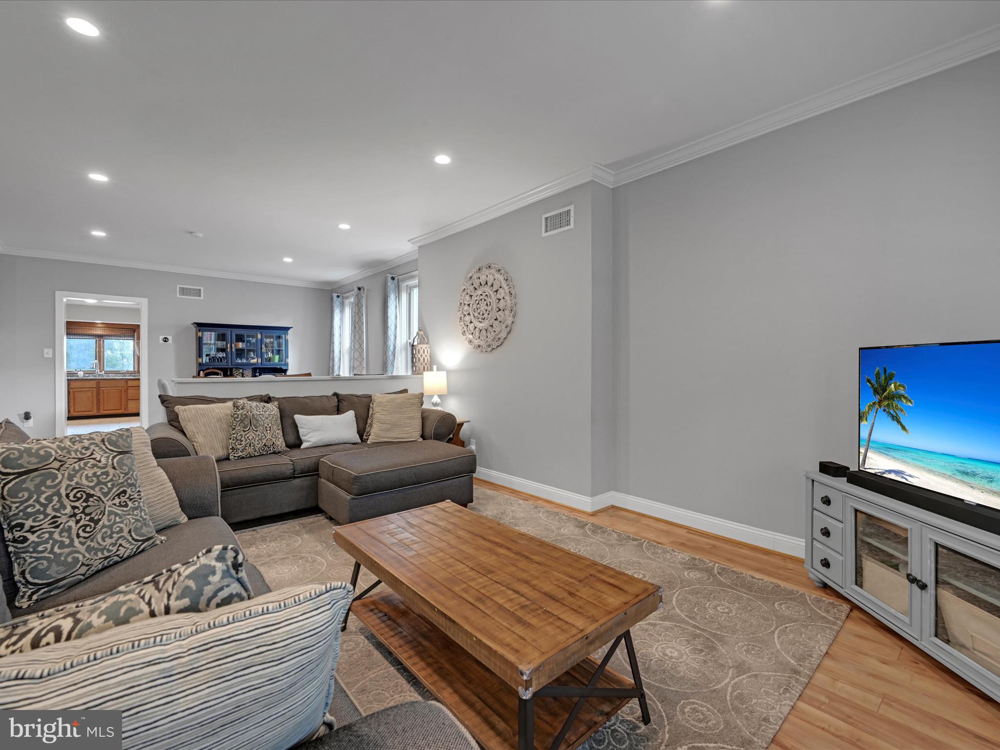 Furnished living room with gray sectional sofas, a wooden coffee table, and an open view toward the kitchen.